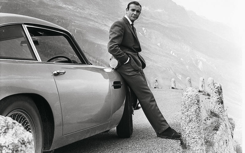 Sean Connery as James Bond leaning onan Aston Martin DB5